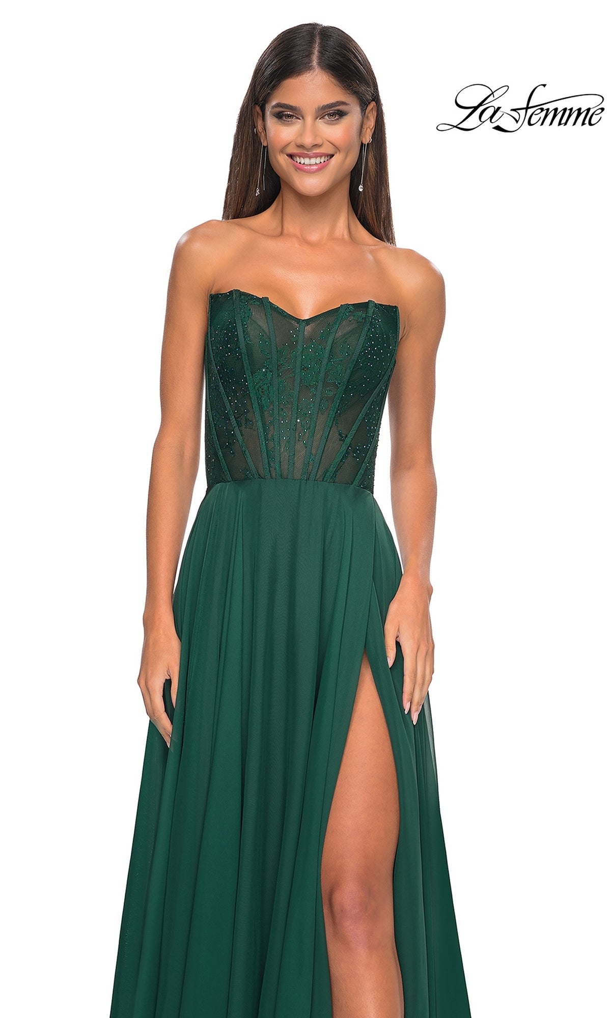 Smiling woman in the La Femme Lace-Bodice Long A-Line Prom Dress 32311, featuring a strapless emerald green sheer corset bodice, high slit, and flowing skirt, stands against a white background.